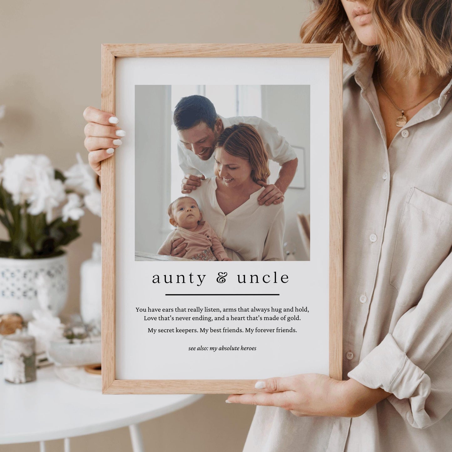 Person holding a framed photo of an auntie & uncle with text, standing in a home setting.
